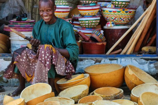 smiling man sitting among stacks of handmade bowls